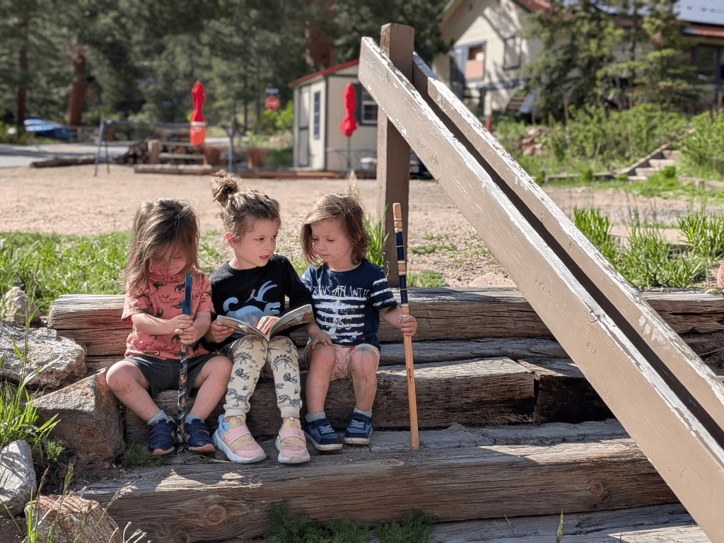 Three children reading together on wooden cabin steps — family-friendly outdoor time at the cabins