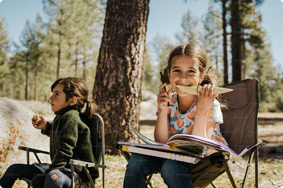Children relaxing in camping chairs in a sunny pine forest — family-friendly outdoor time at the cabins